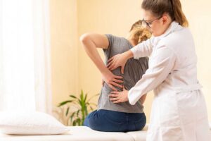 A person gently massaging a sore shoulder while seated at a home desk with natural daylight